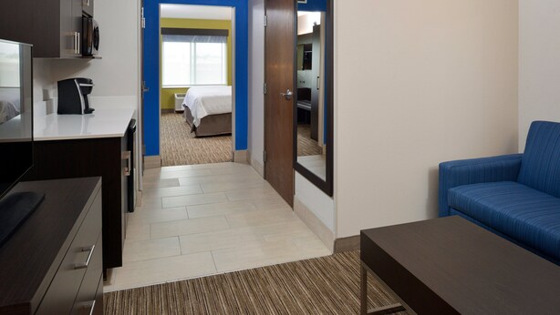 A hotel room with a desk, a blue sofa, a bed, and a bathroom visible through an open door. - Holiday Inn Express & Suites Pueblo North by IHG (Pueblo)