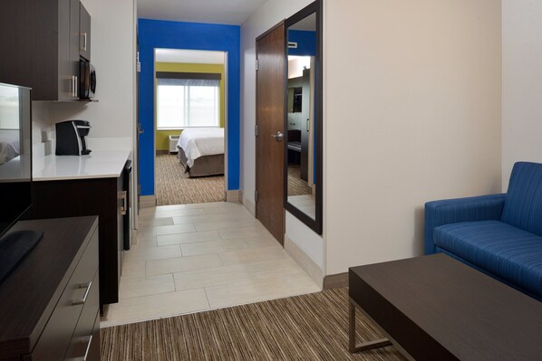 A hotel room with a desk, a blue sofa, a bed, and a bathroom visible through an open door. - Holiday Inn Express & Suites Pueblo North by IHG (Pueblo)