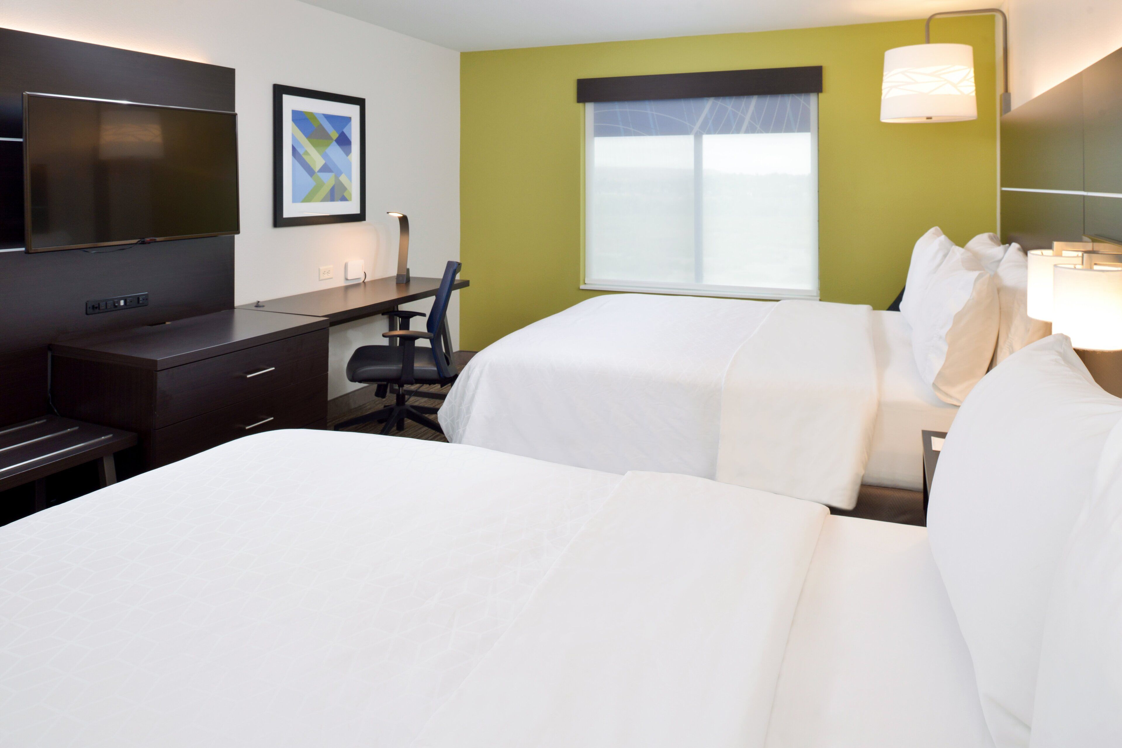 A hotel room with two beds, a desk, a chair, a TV, and a window with a view.