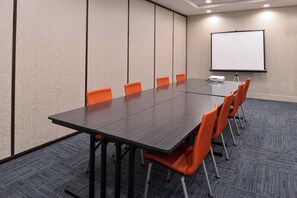 A conference room with a long table, six orange chairs, a projector, and a white screen. - Holiday Inn Express & Suites Pueblo North by IHG (Pueblo)