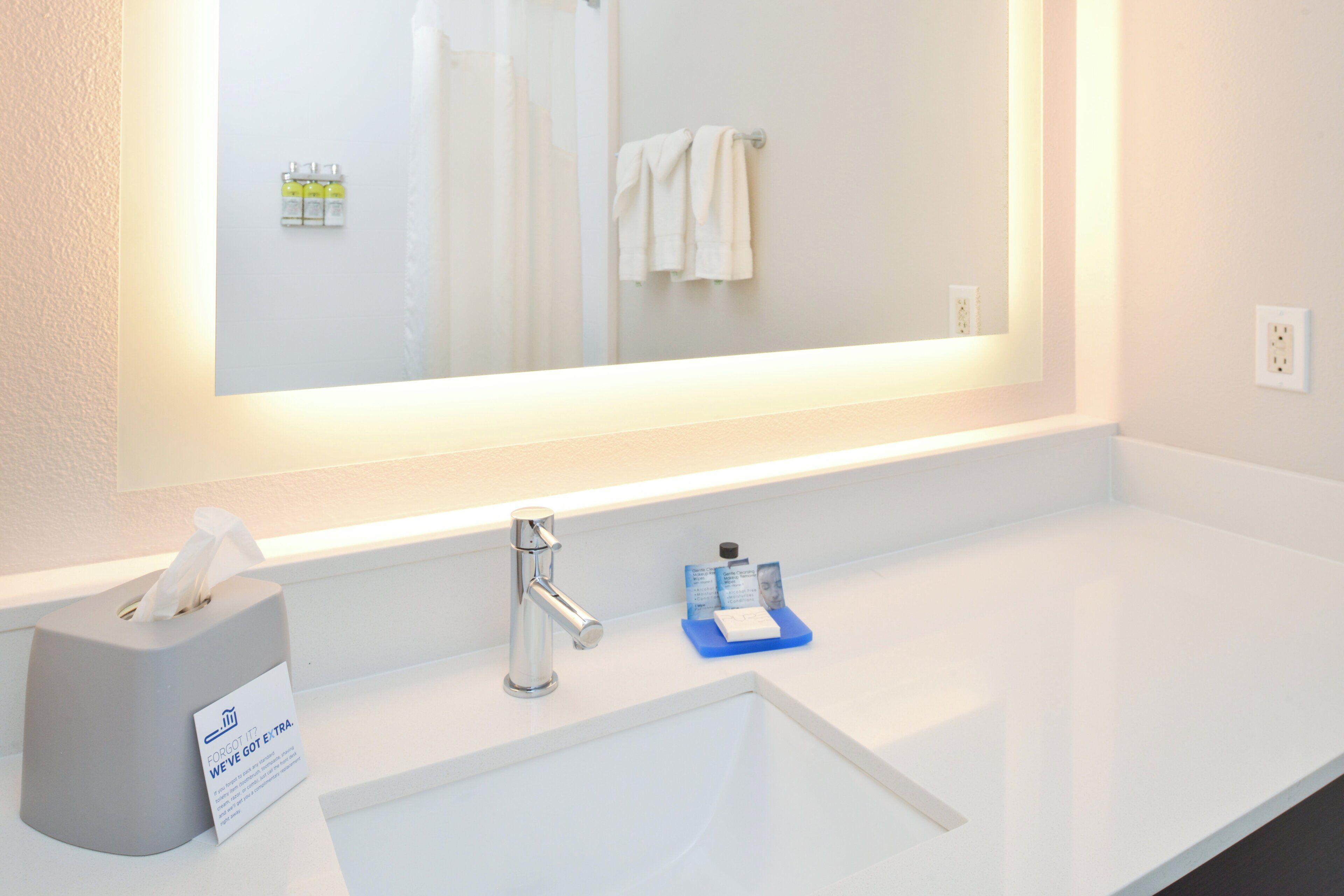 A hotel bathroom with a large mirror, a sink, a tissue box, and a small blue soap dish.