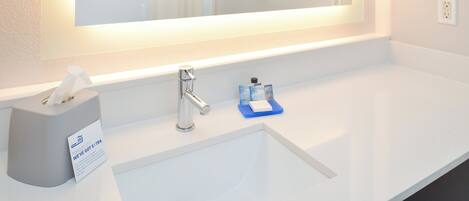 A hotel bathroom with a large mirror, a sink, a tissue box, and a small blue soap dish.