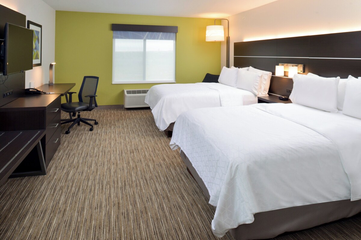 A hotel room with two beds, a desk, a chair, a TV, and a window with blinds.