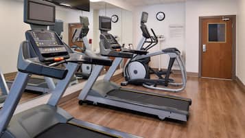 Et fitnesscenter med løbebånd, crosstrainere og et tv ophængt på væggen.