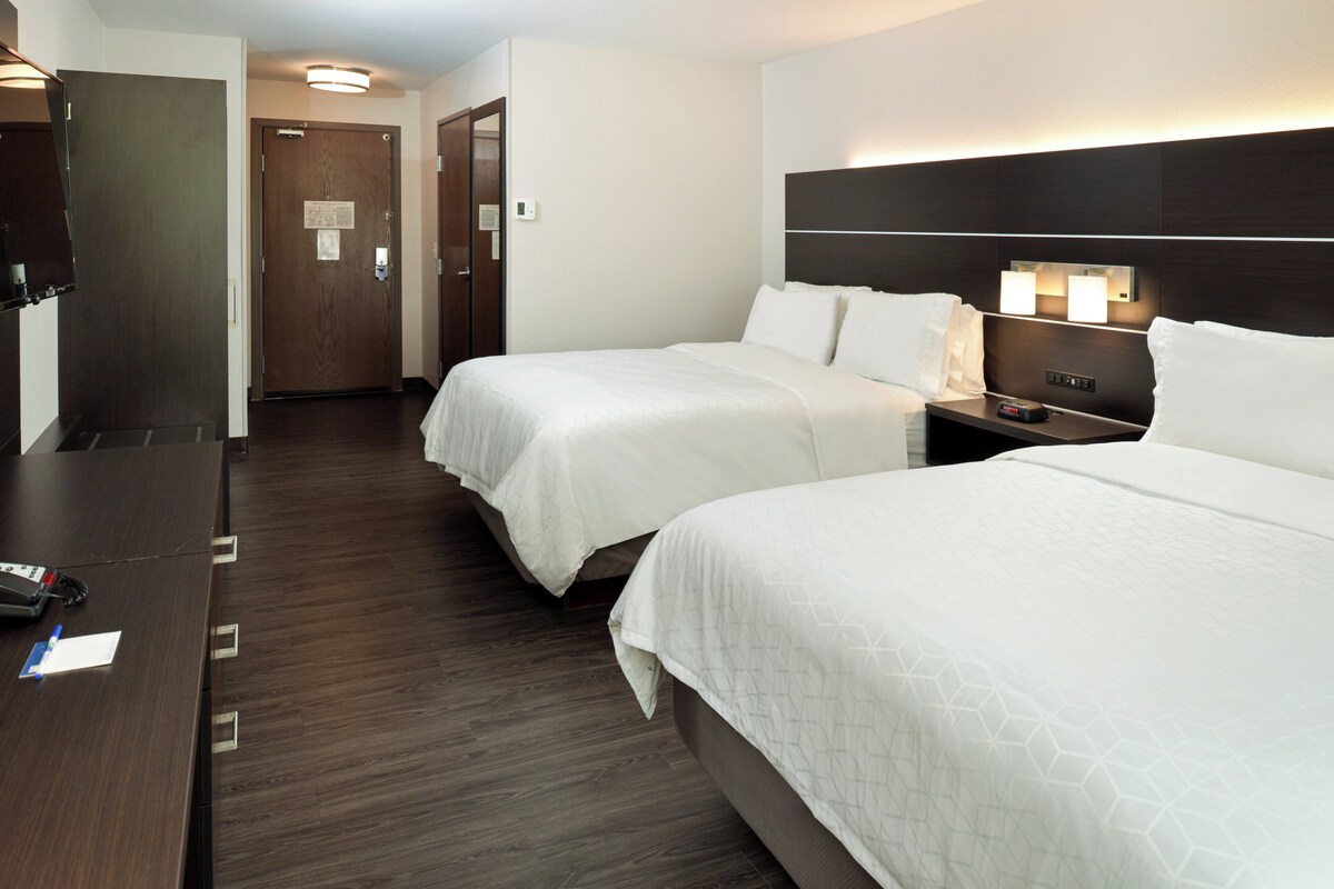 A hotel room with two beds, a desk, a chair, a nightstand, and a door.
