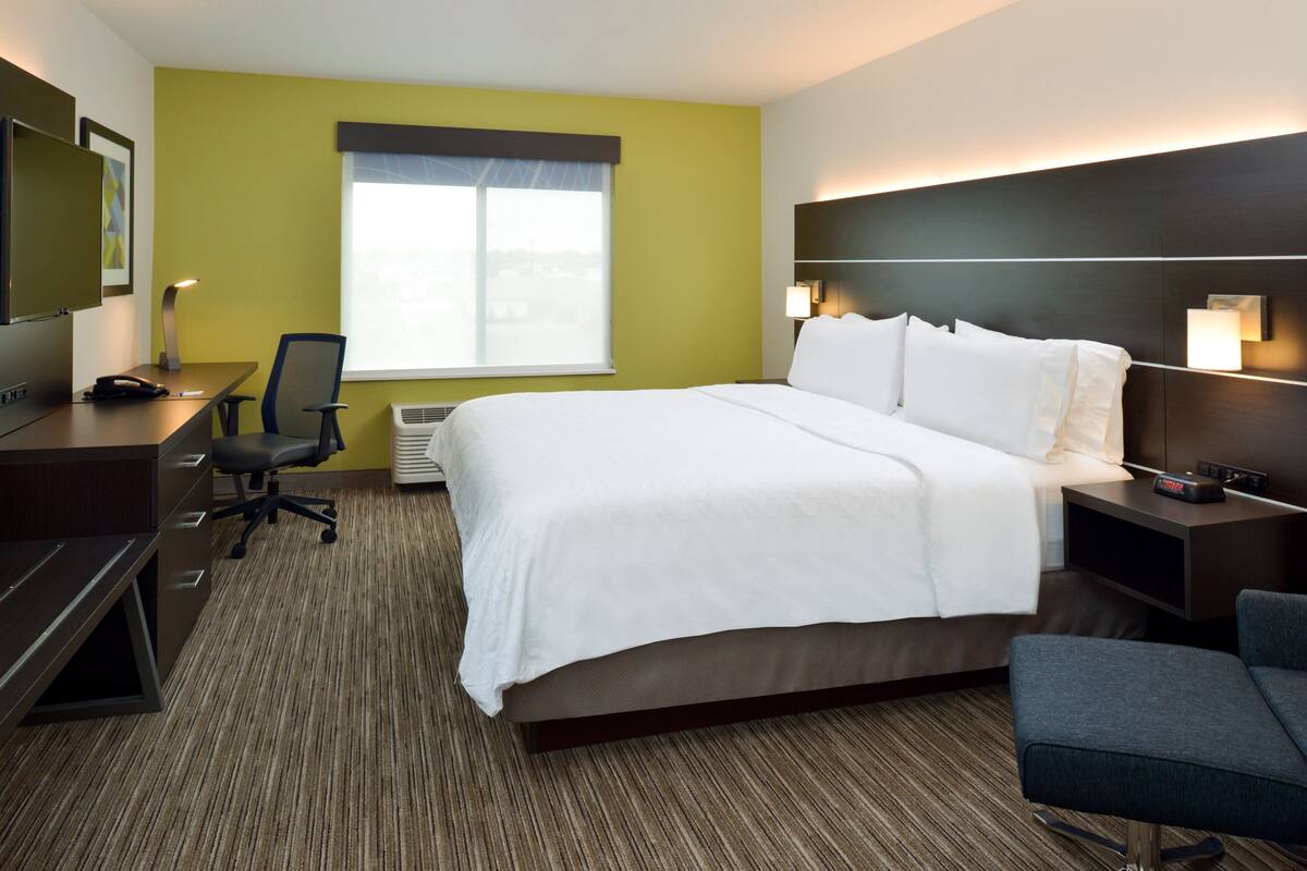 A hotel room with a large bed, a desk, a chair, and a TV.