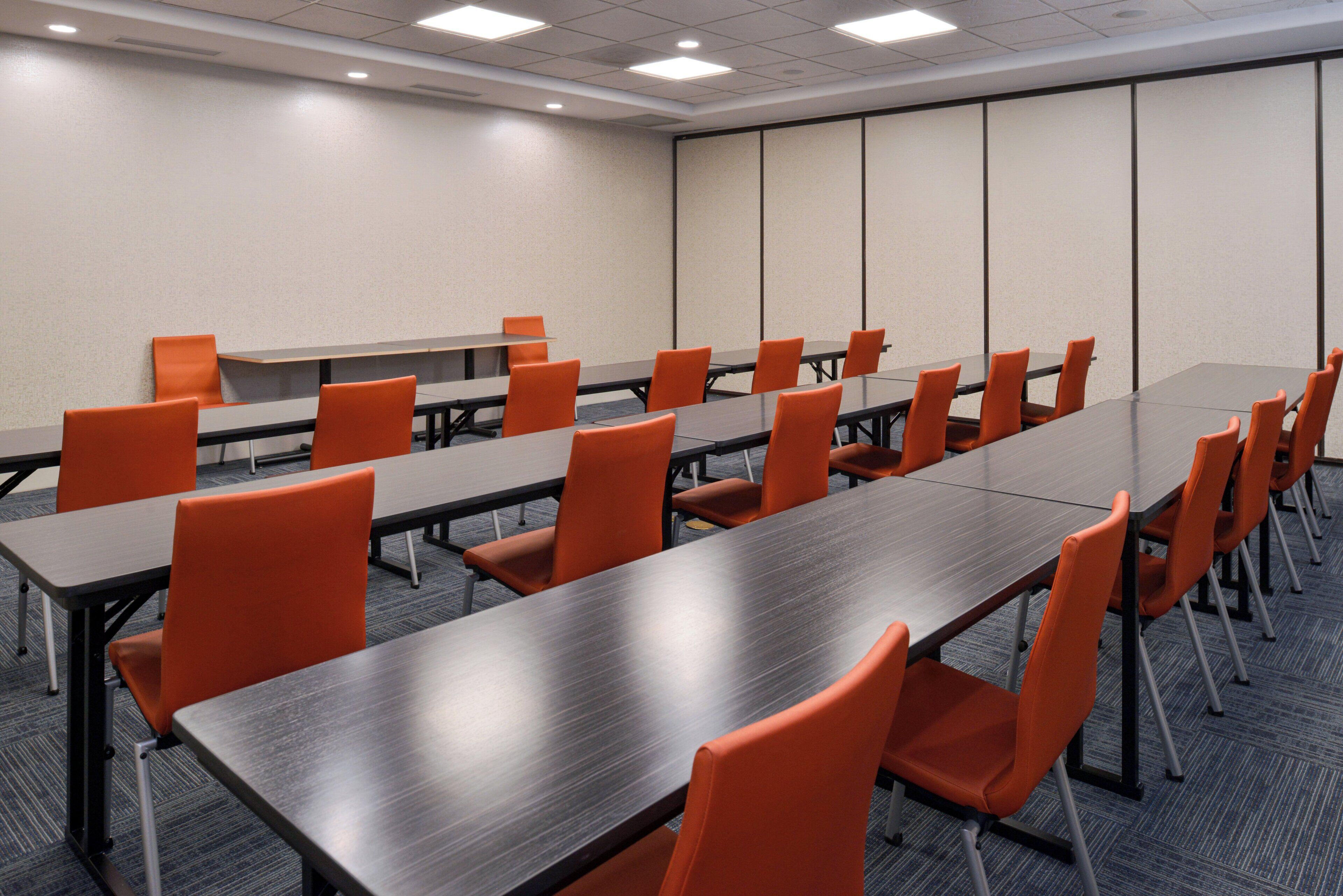 Une salle de conférence dotée de plusieurs tables et chaises, d’un sol recouvert de moquette et d’un mur sobre avec une porte.