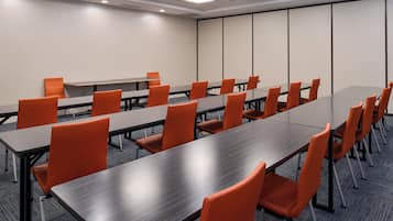 Une salle de conférence dotée de plusieurs tables et chaises, d’un sol recouvert de moquette et d’un mur sobre avec une porte.