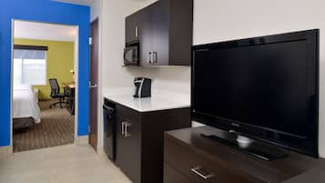 A compact hotel room with a kitchenette, a flat-screen TV, a microwave, and a small dining area.
