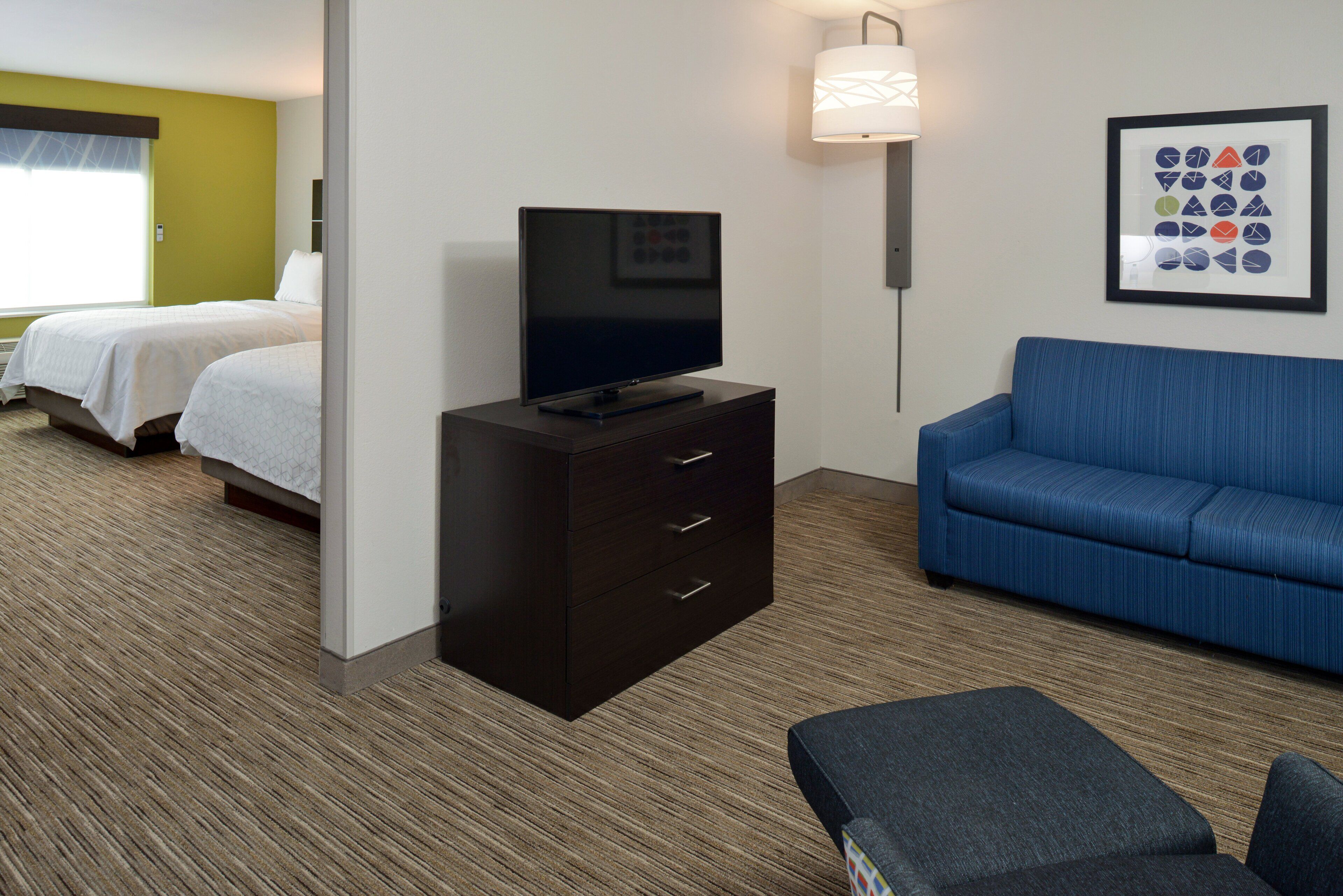 A hotel room with two beds, a flat-screen TV on a dresser, a blue sofa, and a framed picture on the wall.