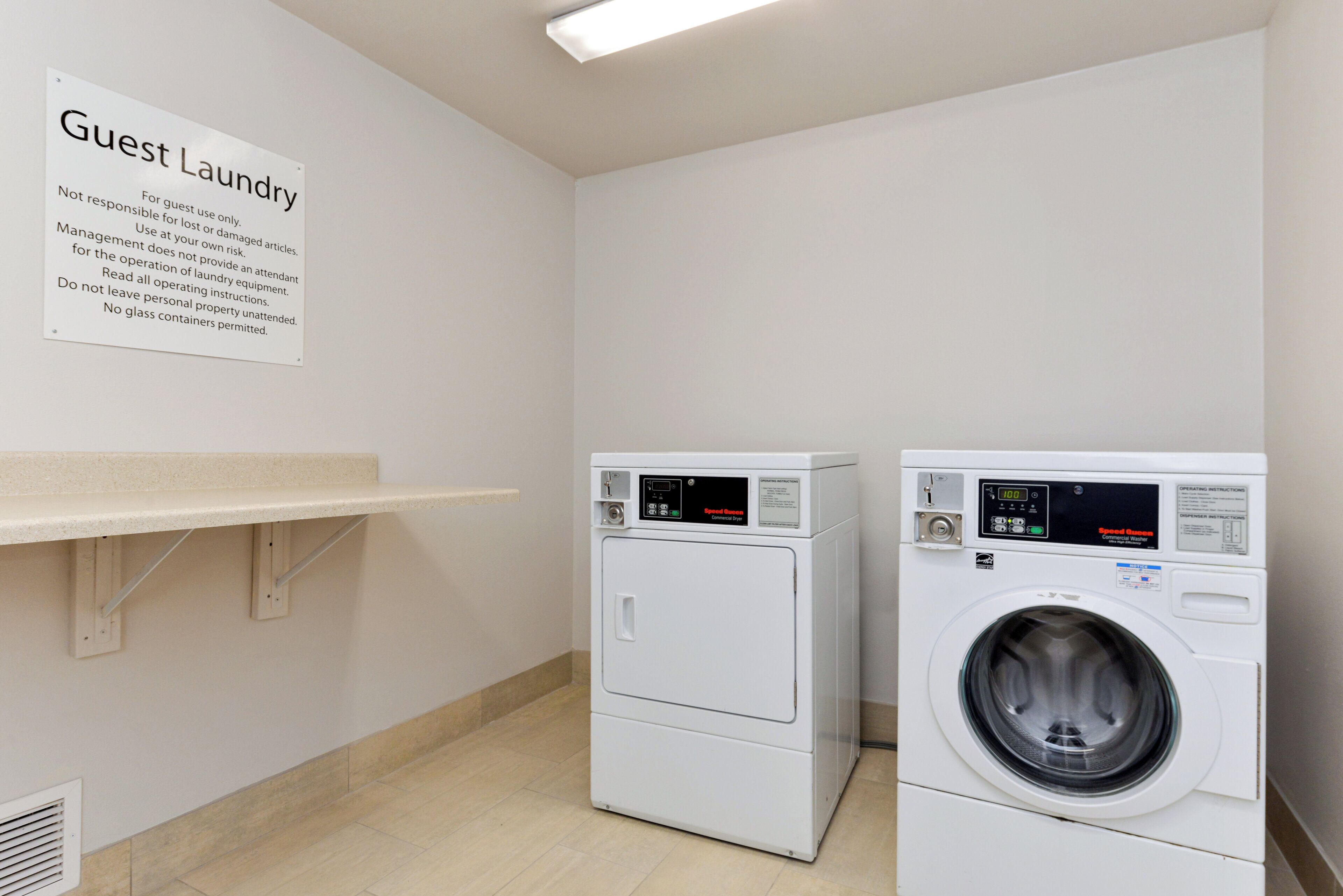 Un espace buanderie à la disposition des clients, comprenant deux machines à laver à chargement frontal, un panneau indiquant les instructions de lavage et une petite étagère.