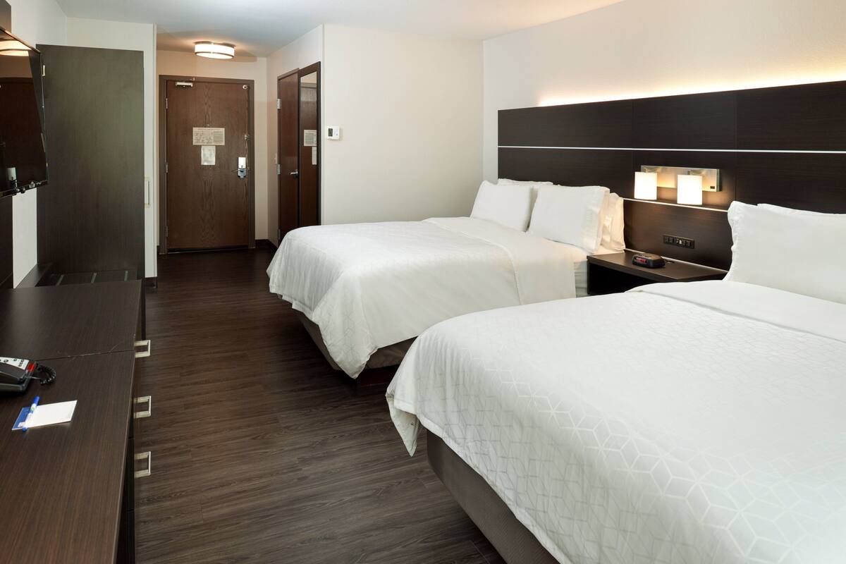 A hotel room with two beds, a desk, and a nightstand with a lamp.