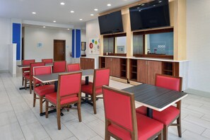 A modern dining area with red chairs and wooden tables, equipped with a flat-screen TV and a blue wall with a clock. - Holiday Inn Express & Suites Pueblo North by IHG (Pueblo)