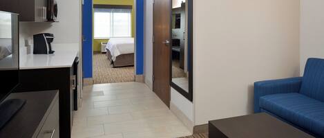 Habitación de hotel con kitchenette, una cama, un sofá azul y una puerta que da a un baño.