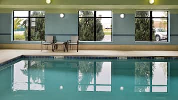 Une piscine avec un bord carrelé, un espace détente avec des chaises, et des fenêtres donnant sur des arbres et un bâtiment.