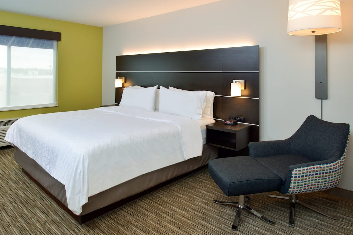 A hotel room with a large bed, a nightstand, a chair, and a wall-mounted lamp.