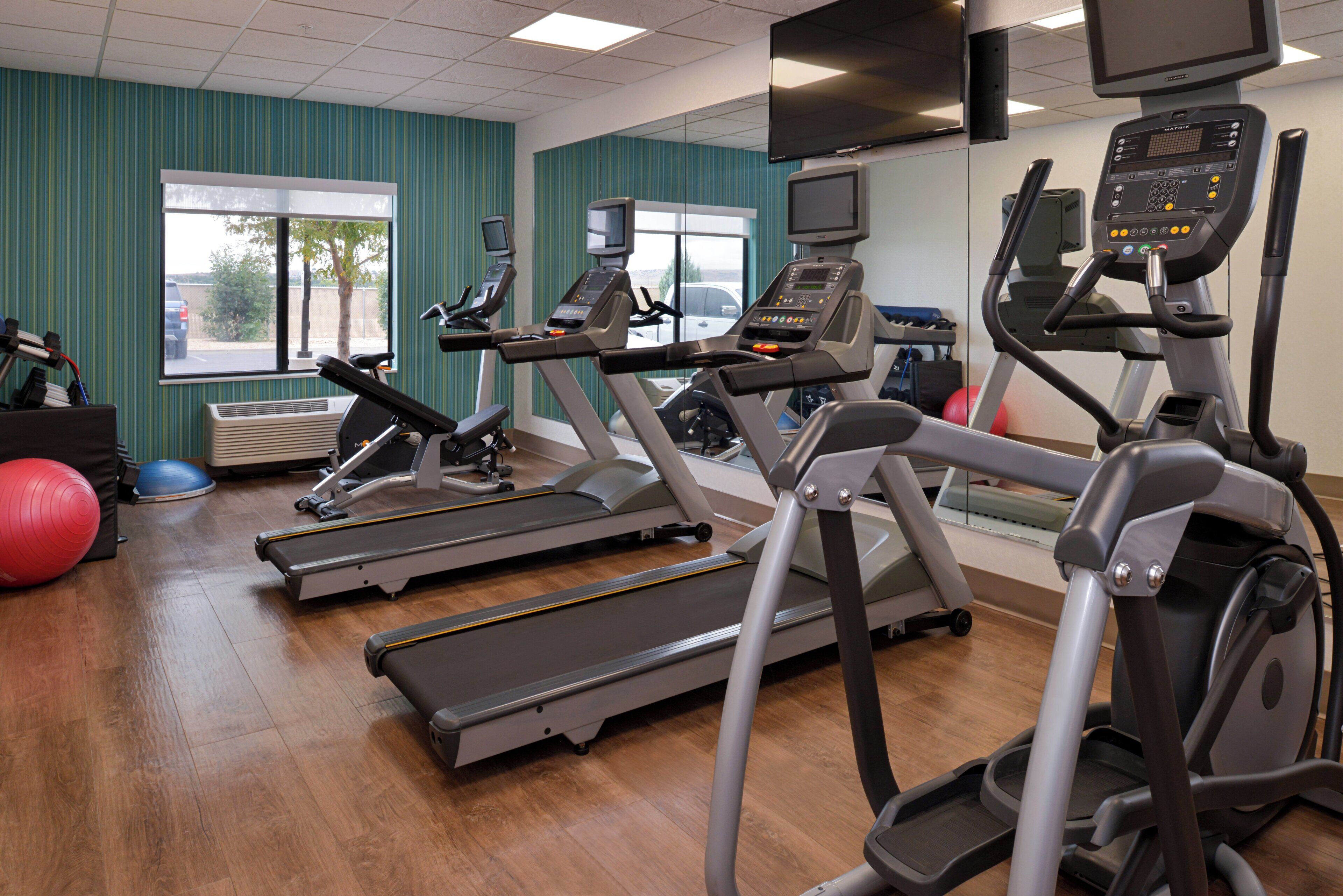 A gym with treadmills, exercise balls, and a television screen.