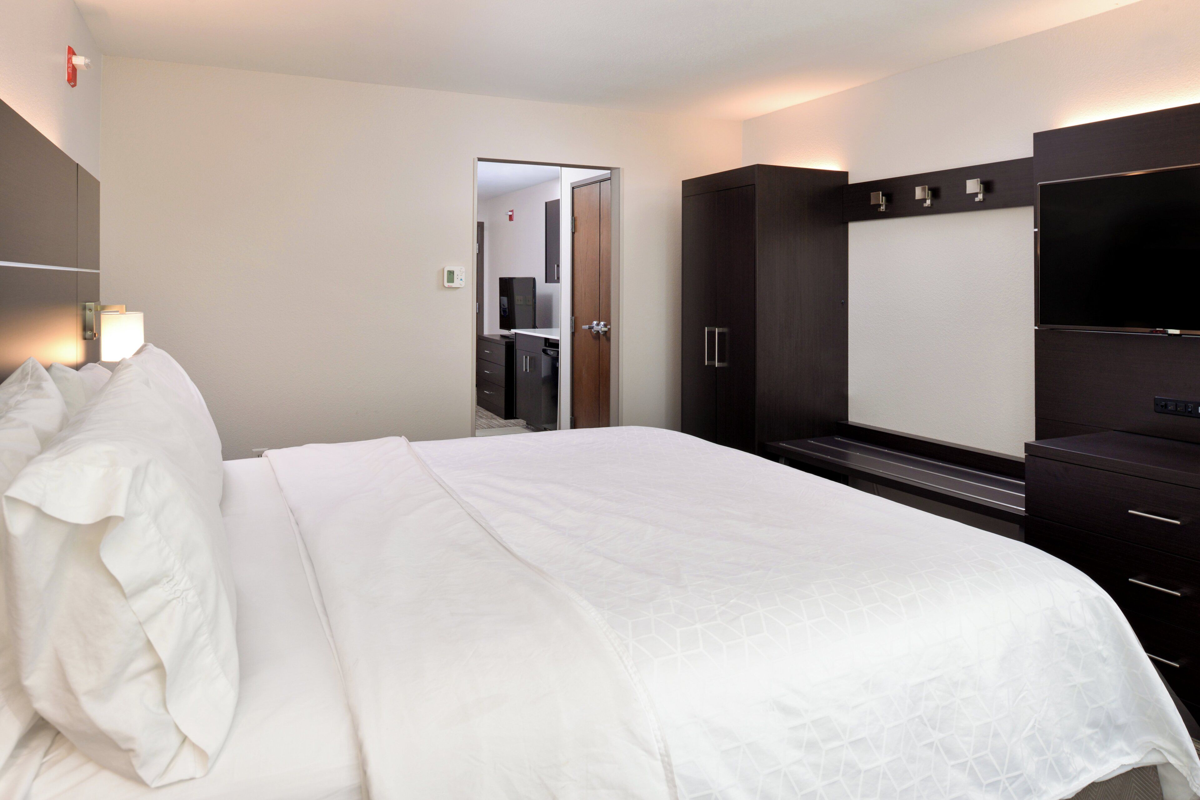 Una habitación de hotel con una cama, televisor, armario y espejo.