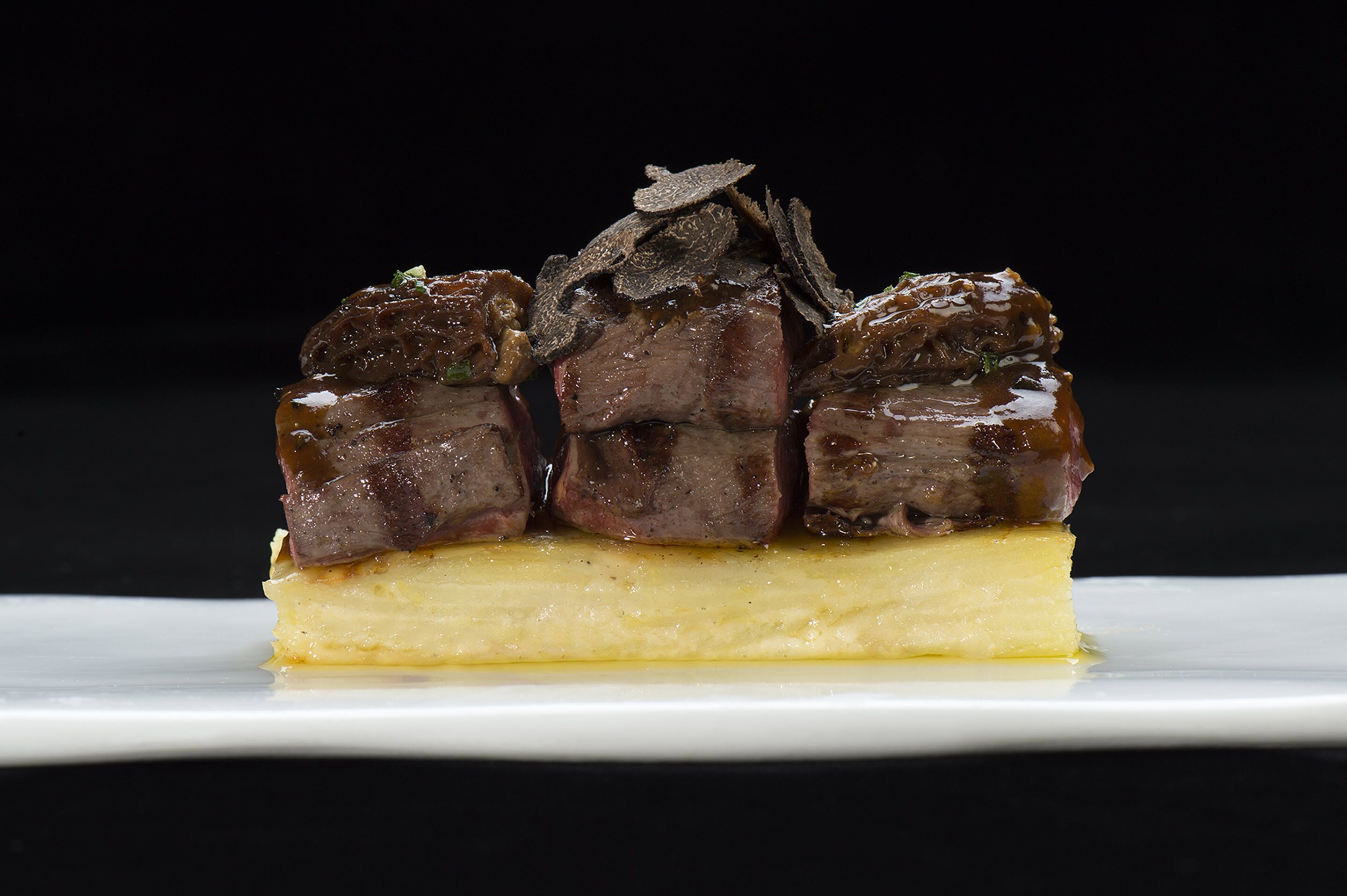 A dessert with three pieces of meat on a creamy base, garnished with herbs, on a white plate.