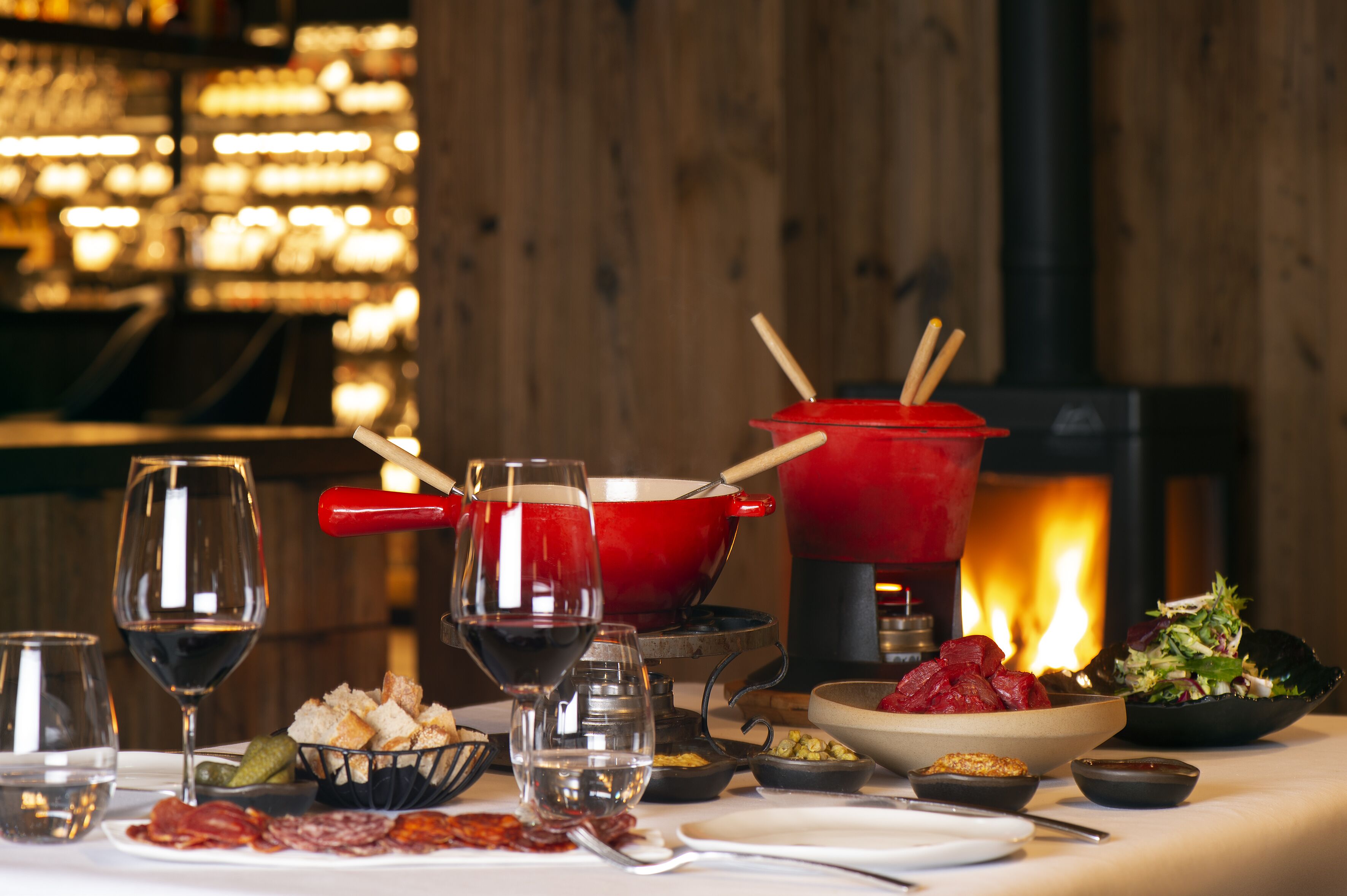 A dining table set with various dishes, glasses of wine, and a red pot with wooden handles.