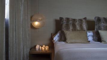 En pænt redt seng med mange puder, et natbord med tændte stearinlys og en kugleformet lampe på væggen.