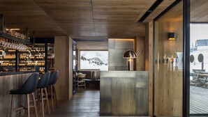 Un área de bar moderna con suelo de madera, taburetes y una vitrina de cristal.