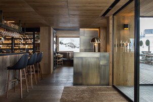 Un área de bar moderna con suelo de madera, taburetes y una vitrina de cristal.