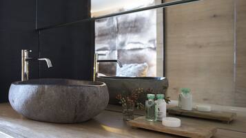 A modern bathroom with a large stone sink, a mirror, and wooden shelves holding toiletries.