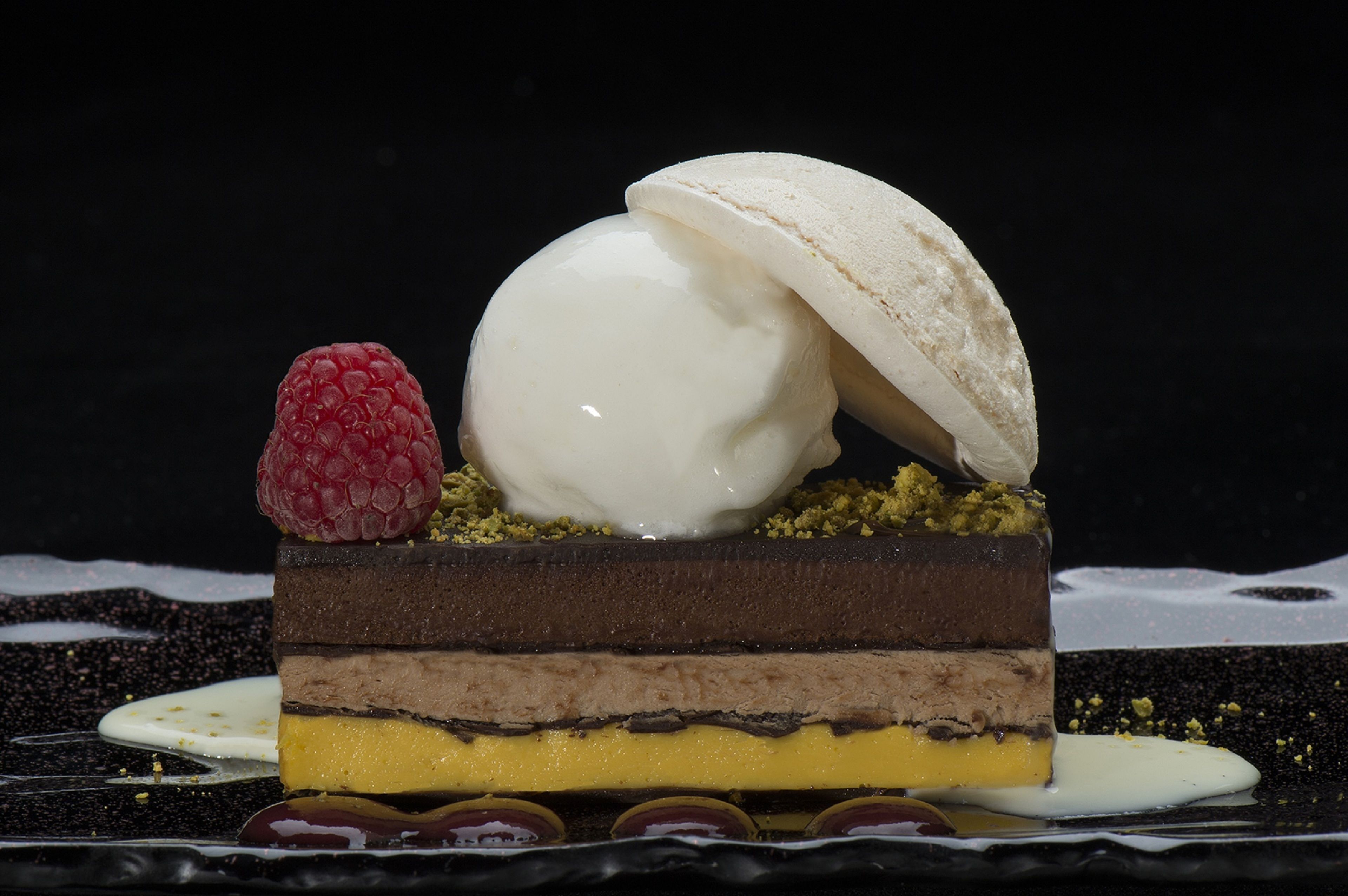 A layered dessert with a raspberry and a scoop of ice cream.