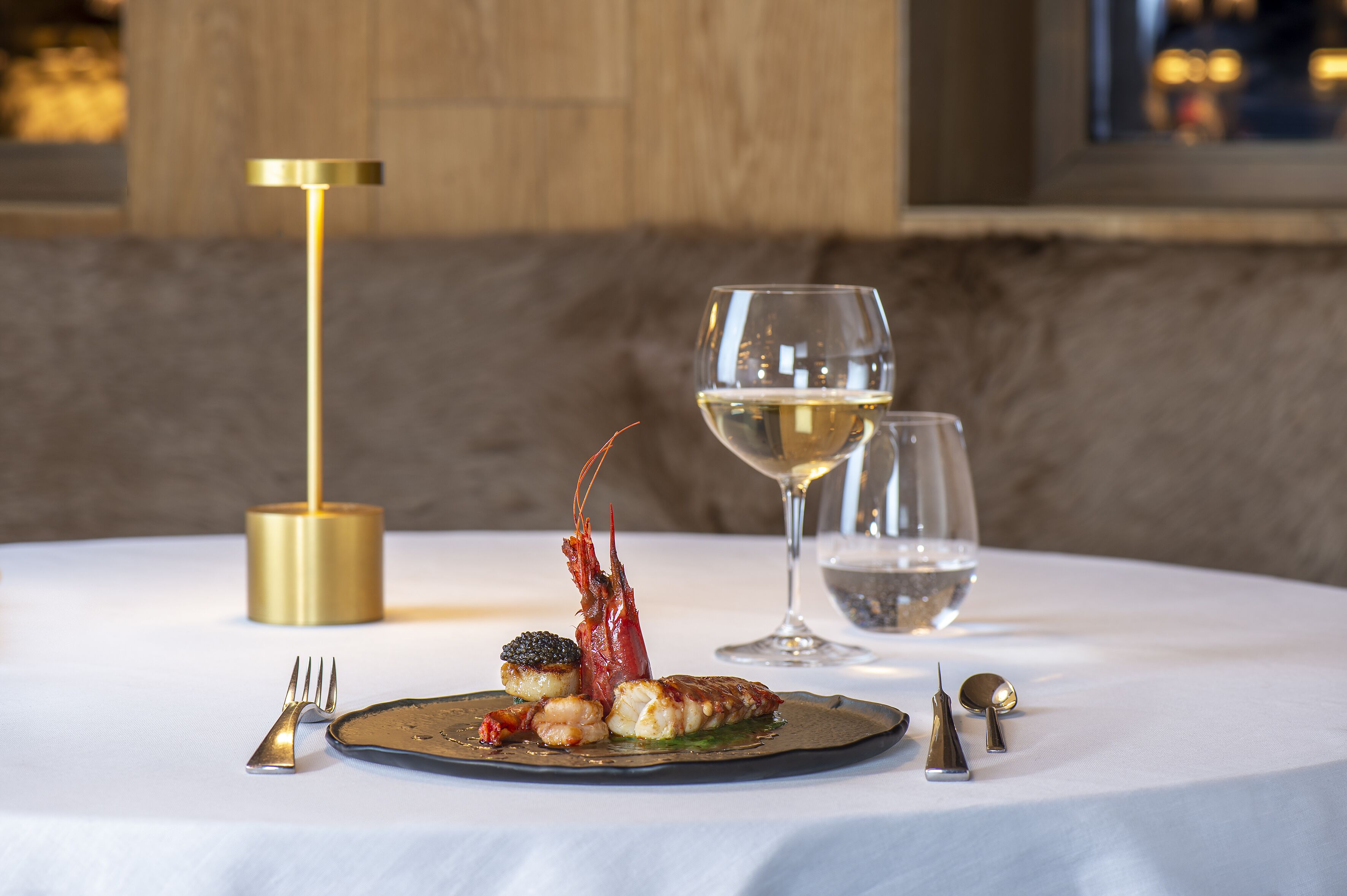 Een eettafel met een visgerecht, een wijnglas en een gouden kandelaar.