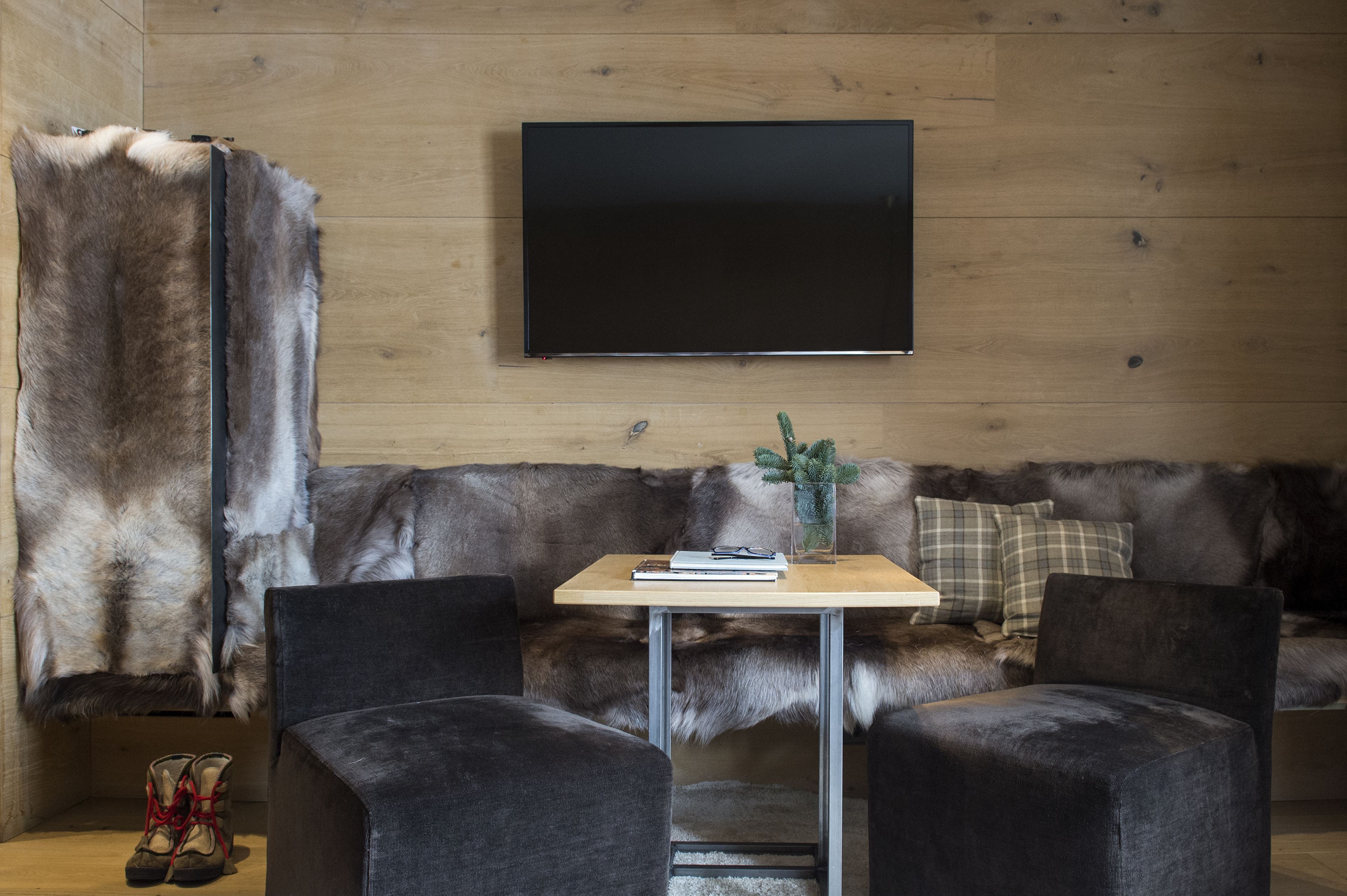 Una habitación con un sofá cubierto de piel, una mesa de madera con un libro y gafas, y un par de botas.