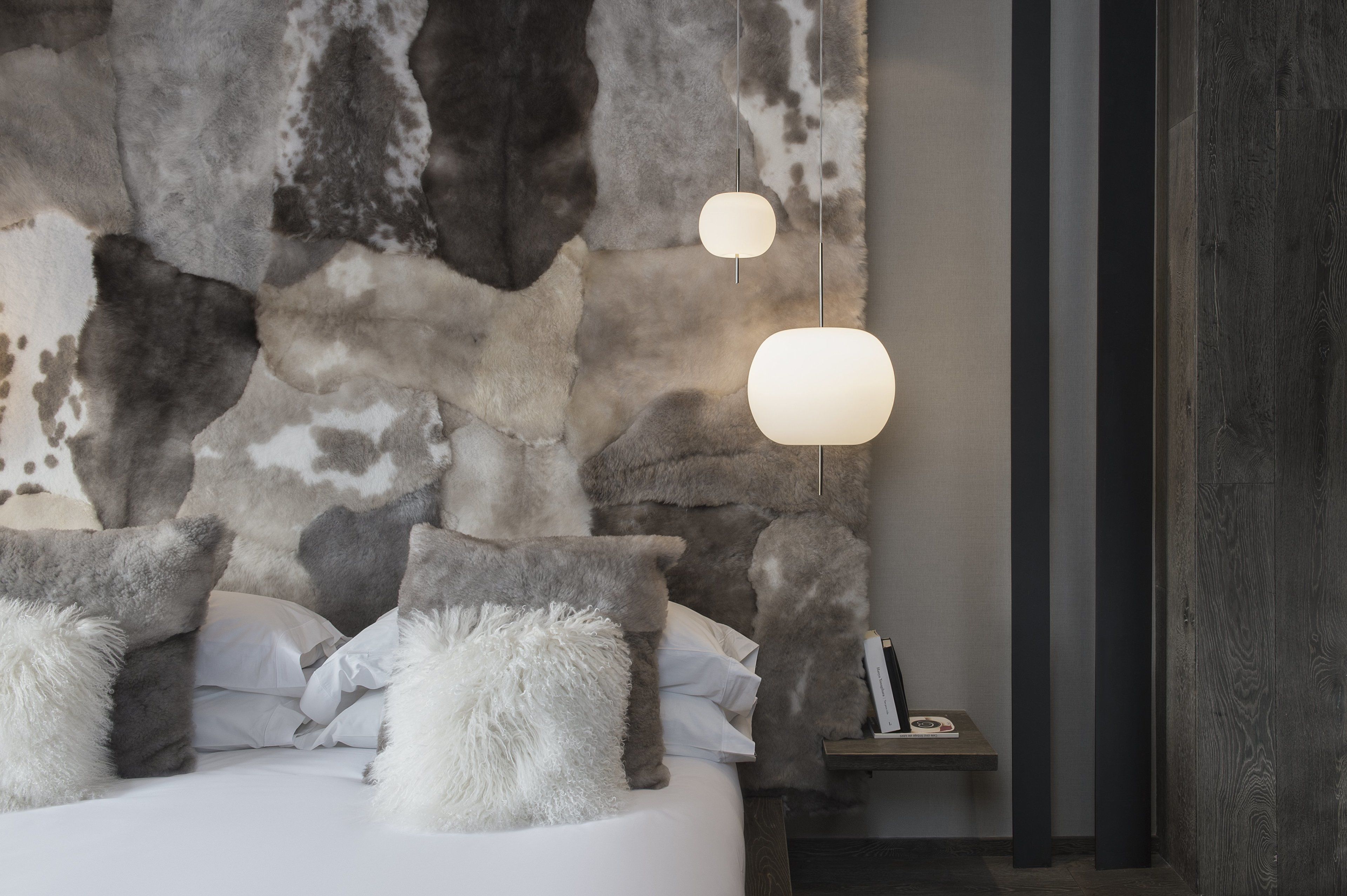 Un dormitorio con pared de piedra, una cama con almohadas mullidas y dos lámparas colgantes.