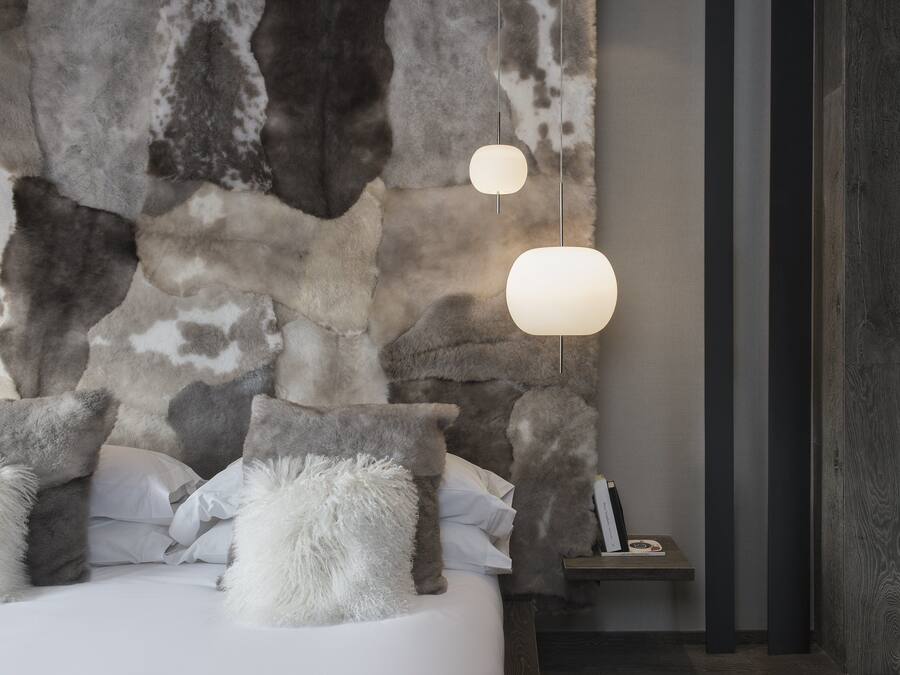 Un dormitorio con pared de piedra, una cama con almohadas mullidas y dos lámparas colgantes.