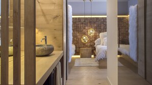 Un baño moderno con un lavamanos de piedra, detalles de madera, una pared de ladrillo y una zona de descanso con una cama y ropa de cama blanca suave.