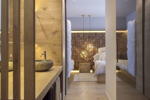 Un baño moderno con un lavamanos de piedra, detalles de madera, una pared de ladrillo y una zona de descanso con una cama y ropa de cama blanca suave.