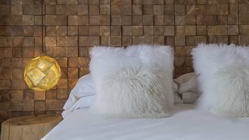 Un lit avec une literie blanche et des oreillers moelleux, adossé à un mur en bois et surmonté d’une lampe suspendue.