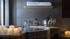 Zona de spa con múltiples velas, una bañera de hidromasaje y un estante con toallas etiquetadas como "GRAUROIG".