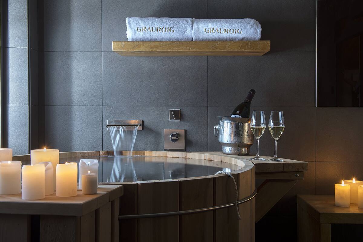 A spa area with multiple candles, a hot tub, and a shelf with towels labeled "GRAUROIG".