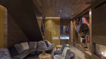 Un intérieur chaleureux et moderne avec un plafond en bois, un canapé d’angle, une cheminée et des étagères à livres.