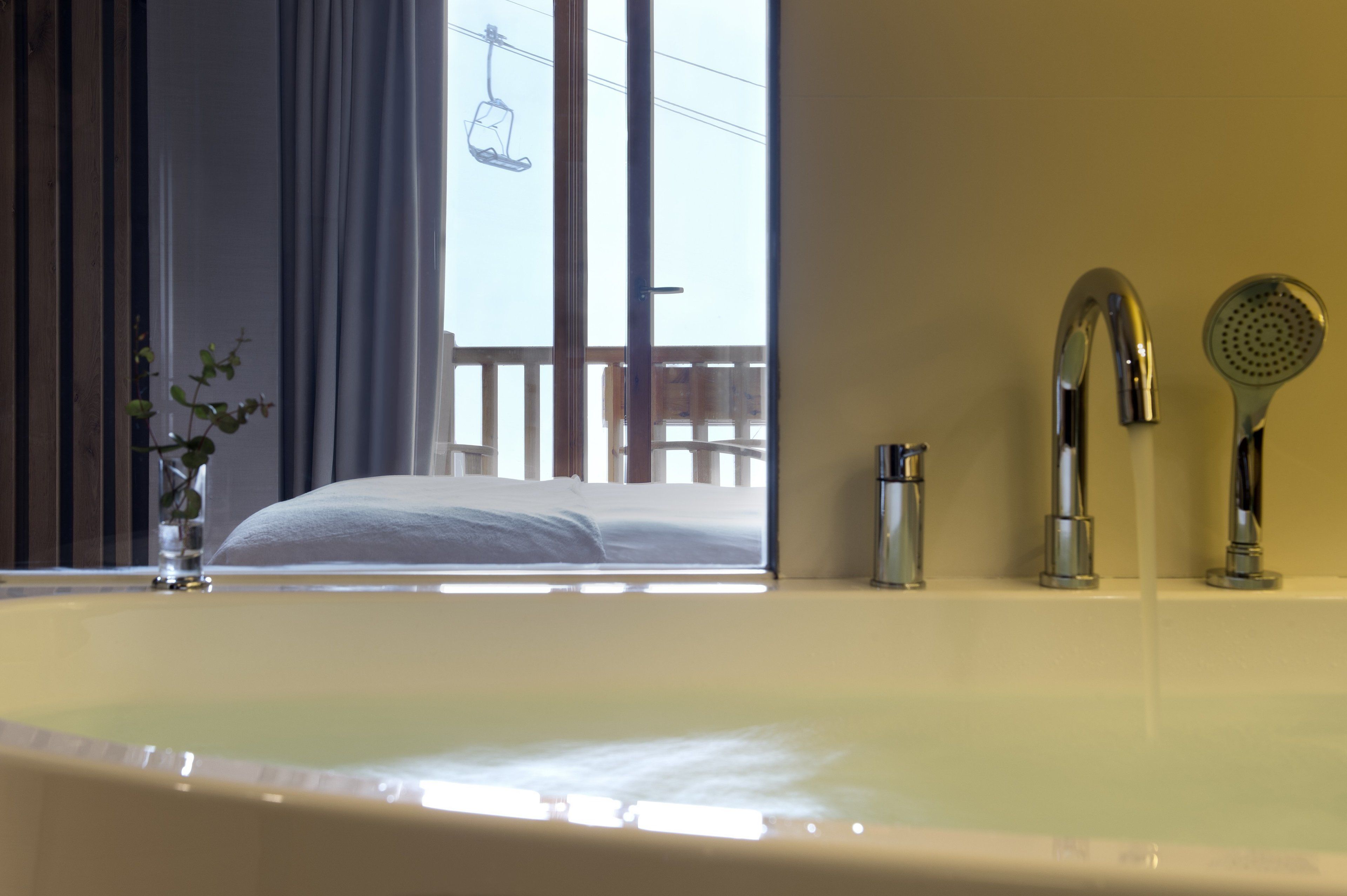 A bathroom with a bathtub, a shower, and a window with a view of a balcony.