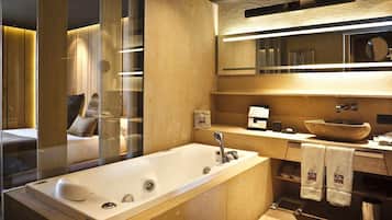 A modern bathroom with a large bathtub, a wooden vanity, a round mirror, and a large sink.