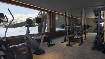 Academia com equipamentos de cardio, máquinas de musculação e vista para uma montanha coberta de neve.