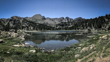 Paisagem montanhosa com um lago, cercado por florestas densas e terreno rochoso.