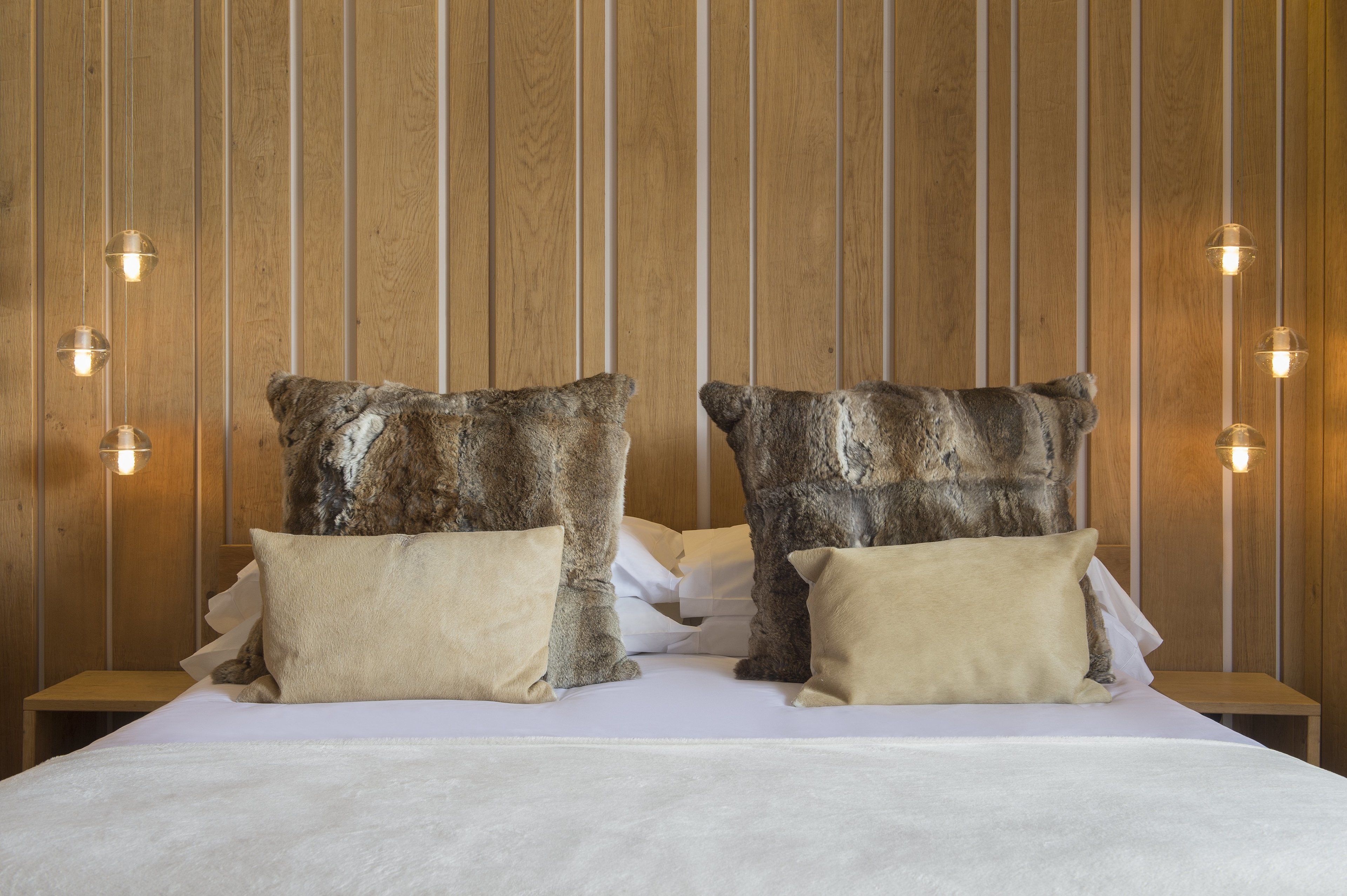 Una cama con dos almohadas grandes y con textura, y un cabecero de madera con líneas verticales.