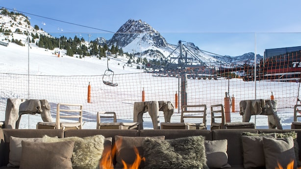 Un rincón acogedor con una chimenea, con vistas a una pista de esquí y una montaña.