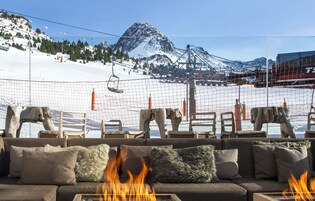 Un rincón acogedor con una chimenea, con vistas a una pista de esquí y una montaña.