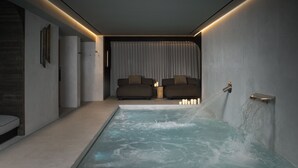 Un spa moderno con un jacuzzi, un sofá y una fuente de agua en la pared.