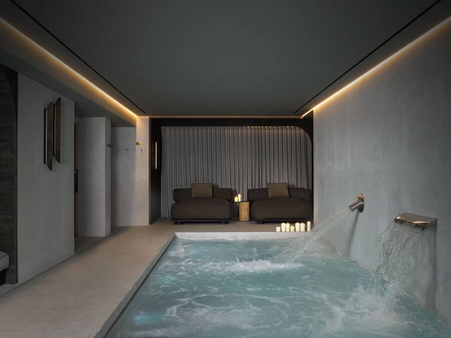 Un spa moderno con un jacuzzi, un sofá y una fuente de agua en la pared.