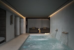 Un spa moderno con un jacuzzi, un sofá y una fuente de agua en la pared.
