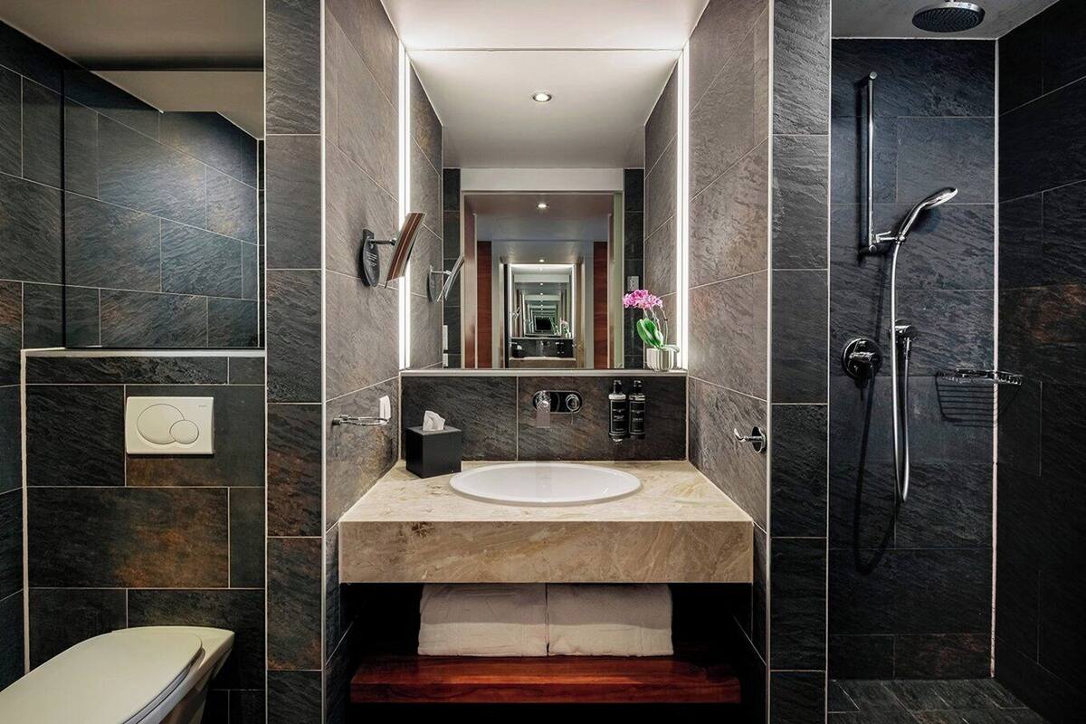 Un baño moderno con lavamanos de mármol, espejo, toallero y ducha.